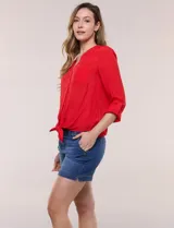 Blusa de calce relajado color salmón, confeccionada en tela liviana con textura sutil. Presenta escote en V con abotonadura frontal, bolsillo parche en el pecho, mangas largas regulables con presilla y ruedo con opción de anudar en el frente.
