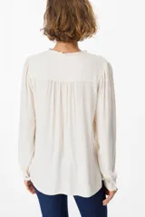 Camisa de manga larga color azul, con cuello mao y detalle de volados en la botonadura frontal. Presenta puños abotonados y un corte recto y fluido.