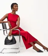 Vestido midi sin mangas color rojo, confeccionado en microfibra con elastano. Presenta un diseño drapeado en el lateral de la cintura con un adorno metálico en forma de gota, escote redondo y una abertura lateral en la falda.
