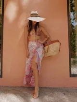 Falda playera larga estilo pareo, confeccionada en gasa estampada con diseño de algas marinas en tonos rosa, celeste, verde y blanco. Presenta cinturón anudado en la cintura y volantes en la abertura y el bajo.