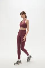 Calza deportiva de tiro alto y ajuste ceñido al cuerpo, confeccionada en tejido elástico de color bordó.