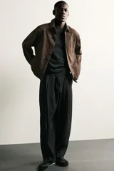 Pantalón de corte balloon fit en color gris oscuro, confeccionado en tejido con viscosa. Presenta pliegues frontales, cintura ajustable con cinturón integrado, bolsillos laterales y bolsillos traseros de doble vivo. Cierre frontal con cremallera y botón.