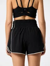 Short negro deportivo de tiro alto con pretina ancha elastizada, cordón de ajuste y detalles de ribetes blancos en los laterales y dobladillo. Incluye short interior integrado.