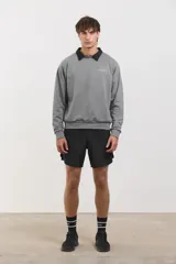 Buzo de algodón rústico color gris melange, con cuello redondo y cuello tipo polo negro superpuesto. Presenta el logo de la marca bordado en el pecho y puños acanalados.