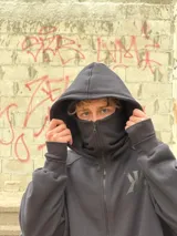 Campera oversize negra de felpa suave con cierre frontal, doble capucha que incluye un diseño tipo balaclava integrado, bolsillos laterales y logo bordado tono sobre tono en el pecho.