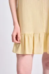 Vestido corto amarillo sin mangas, confeccionado en lino, con cuello con lazo y volados en el ruedo.