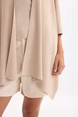 Ruana de punto color beige con hilos de lurex incorporados, diseño abierto y caída fluida.