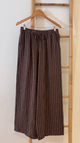 Pantalón de corte ancho y relajado, confeccionado en lino con diseño de rayas verticales. Presenta cintura elástica con cordón de ajuste y bolsillos laterales.