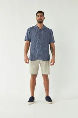 Camisa de manga corta con cuello cubano, confeccionada en viscosa con estampado de hojas en tonos azules. Presenta cierre frontal abotonado y corte slim.