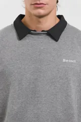 Buzo de algodón rústico color gris melange, con cuello redondo y cuello tipo polo negro superpuesto. Presenta el logo de la marca bordado en el pecho y puños acanalados.