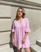 Vestido corto rosa con estampado de cuadrillé, escote en V, mangas cortas con volados y botones decorativos.