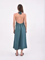 Vestido midi de color verde petróleo, con escote halter cruzado y espalda descubierta. Presenta un corte entallado en la cintura y falda con vuelo.