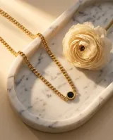 Collar de cadena tipo eslabones gruesos con baño de oro, que presenta un dije central circular con incrustación de piedra ónix negra.