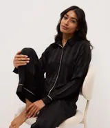 Pijama largo Lov de dos piezas confeccionado en satén negro con rayas sutiles y detalles de vivo en contraste. Consta de una camisa de manga larga con cuello y solapa, abotonado frontal, y un pantalón de calce amplio con cintura elastizada.