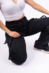 Pantalón cargo negro de jeans sin lycra, corte holgado y tiro alto. Cuenta con múltiples bolsillos laterales con solapa y cordones ajustables.