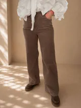 Pantalón de pana color tostado con corte wide leg y tiro alto. Presenta diseño clásico de cinco bolsillos, cierre frontal con botón y una caída recta y amplia.