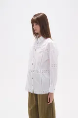 Camisa de algodón color blanco, de corte holgado y manga larga. Presenta detalles de encaje tipo puntilla en el frente, espalda y mangas, con cierre frontal de botones y cuello camisero clásico.