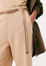 Pantalón recto color beige de tiro medio, con bolsillos laterales y un cinturón fino integrado con detalle de nudos en la parte delantera.