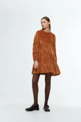 Vestido corto de terciopelo color tostado, con diseño de tres niveles con volados, cuello redondo con detalle de fruncido y mangas largas con volados aplicados.