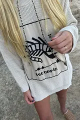 Sweater de punto negro con diseño oversize, cuello redondo y manga larga. Presenta un bordado frontal en color crudo con motivo del signo del zodíaco Géminis, acompañado de detalles de sol, luna y estrellas dentro de un recuadro.