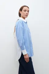 Camisa celeste con rayas verticales blancas, de corte amplio y cuello camisero clásico. Presenta bolsillo de parche en el pecho, espalda lisa en color blanco y puños abotonados.