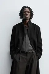 Abrigo negro de corte recto confeccionado en tejido con lana. Tiene cuello alto, manga larga con puños abotonados, bolsillos laterales y abertura en la espalda. Cierre frontal con botones.