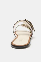 Sandalia plana de color beige con dos tiras ajustables mediante hebillas metálicas doradas. Presenta un diseño de punta redonda y suela plana con borde en contraste.