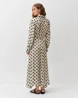 Vestido camisero largo de viscosa y seda, color blanco con estampado de lunares negros. Presenta cuello camisero, mangas largas abullonadas y un cinturón ajustable del mismo género.