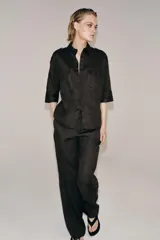 Pantalón flare de tiro medio confeccionado en lino color marrón. Cuenta con cintura con trabillas, bolsillos delanteros, perneras de corte evasé y cierre frontal con cremallera y botón.