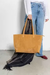 Bolso tipo tote de gamuza color tostado, con doble asa de hombro y cierre superior con cremallera.