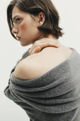 Jersey de punto color gris oscuro, con escote recto tipo off-shoulder, manga larga y detalle de aplique metálico en el hombro. Presenta acabados en rib en puños y ruedo.