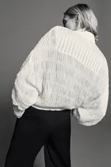 Bomber de viscosa color blanco crudo, de corte holgado, cuello subido y cierre frontal con cremallera. Presenta mangas abullonadas con puños ajustados y detalle de tejido satinado en la parte superior delantera.