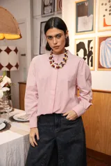 Camisa de corte clásico con cuello mao y cierre frontal oculto, confeccionada en tela de algodón con estampado de rayas verticales finas en color rojo y blanco. Presenta mangas largas con puños abotonados.