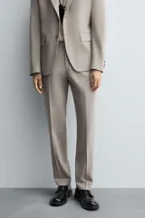 Pantalón de vestir slim fit en color beige, confeccionado en tejido con lana. Presenta cierre frontal con cremallera y botón, bolsillos laterales y bolsillos traseros de doble vivo con botón.