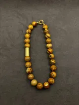 Collar de cuentas de piedras naturales en tonos tierra, con detalles de tubos dorados en los laterales.
