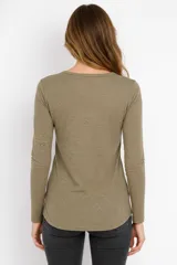 Remera blanca de manga larga, entallada, con cuello redondo y una hilera de botones en el frente. Incluye un pequeño bolsillo decorativo en el pecho.