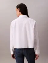 Camisa blanca de algodón y elastano, con cuello clásico de punta, cierre frontal con botones y mangas largas con puños abotonados.