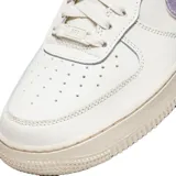 Championes Nike Air Force 1 de corte bajo, con cuerpo de cuero blanco, suela de goma color crema y detalles en tono lila metalizado en el swoosh lateral y el talón.