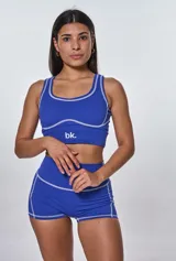 Conjunto deportivo compuesto por un top de escote redondo y un short de tiro alto, ambos en color azul con costuras decorativas a la vista en color blanco. El top presenta el logo de la marca estampado en el frente.