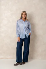 Camisa de manga larga en color blanco, confeccionada en tejido traslúcido con delicados bordados florales en hilo de seda al tono. Presenta cuello clásico, cierre frontal con botones y puños abotonados.