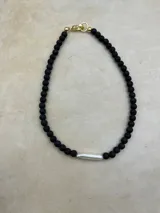 Collar artesanal compuesto por cuentas de piedra volcánica en diversos tonos y tamaños, con una perla natural de río como dije central y cierre metálico dorado.