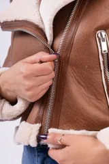 Campera tipo gamulán de cuerina color beige con interior y detalles en corderito blanco. Presenta corte biker, cierre frontal diagonal, bolsillos laterales con cierre y puños con vuelta de corderito.