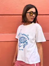 Remera blanca de corte holgado con estampa frontal en color azul que ilustra una escena de aperitivo con botella, copa y plato, acompañada por la palabra 'aperitivo' y la hora '13:00 PM'.