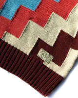 Sweater de cuello alto confeccionado en tejido de punto con diseño geométrico en bloques de colores bordó, rojo, celeste y beige. Presenta puños y ruedo acanalados y un pequeño parche decorativo en el frente.