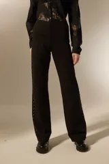 Pantalón tipo calza flare de tiro alto, color negro, con detalle de tachas metálicas plateadas a lo largo de las costuras laterales.
