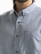 Camisa celeste y blanca a cuadros con cuello abotonado, manga larga y bolsillo en el pecho.