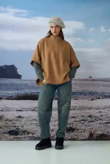 Poncho tejido color marrón, con cuello alto y cierre frontal parcial. Presenta un diseño holgado con aberturas laterales para los brazos.