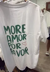 Remera blanca de manga corta y corte holgado con un estampado frontal que incluye una botella de vino, una copa de vino y la palabra "VINO" escrita al revés.