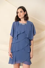 Vestido corto de gasa en color azul, compuesto por un vestido sin mangas con escote redondo decorado con pedrería y una capa corta superpuesta con mangas anchas y diseño en capas escalonadas.
