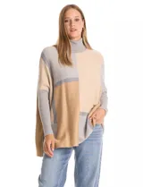 Polera tipo poncho de corte oversize, con cuello alto tejido y mangas largas con puños elásticos. Presenta un diseño geométrico de bloques de color en tonos beige, gris y tostado.